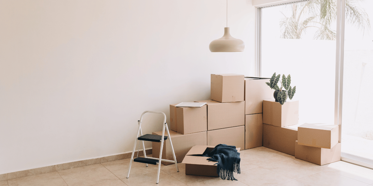 moving boxes in the corner of an apartment near a sliding glass door with sunlight shining through